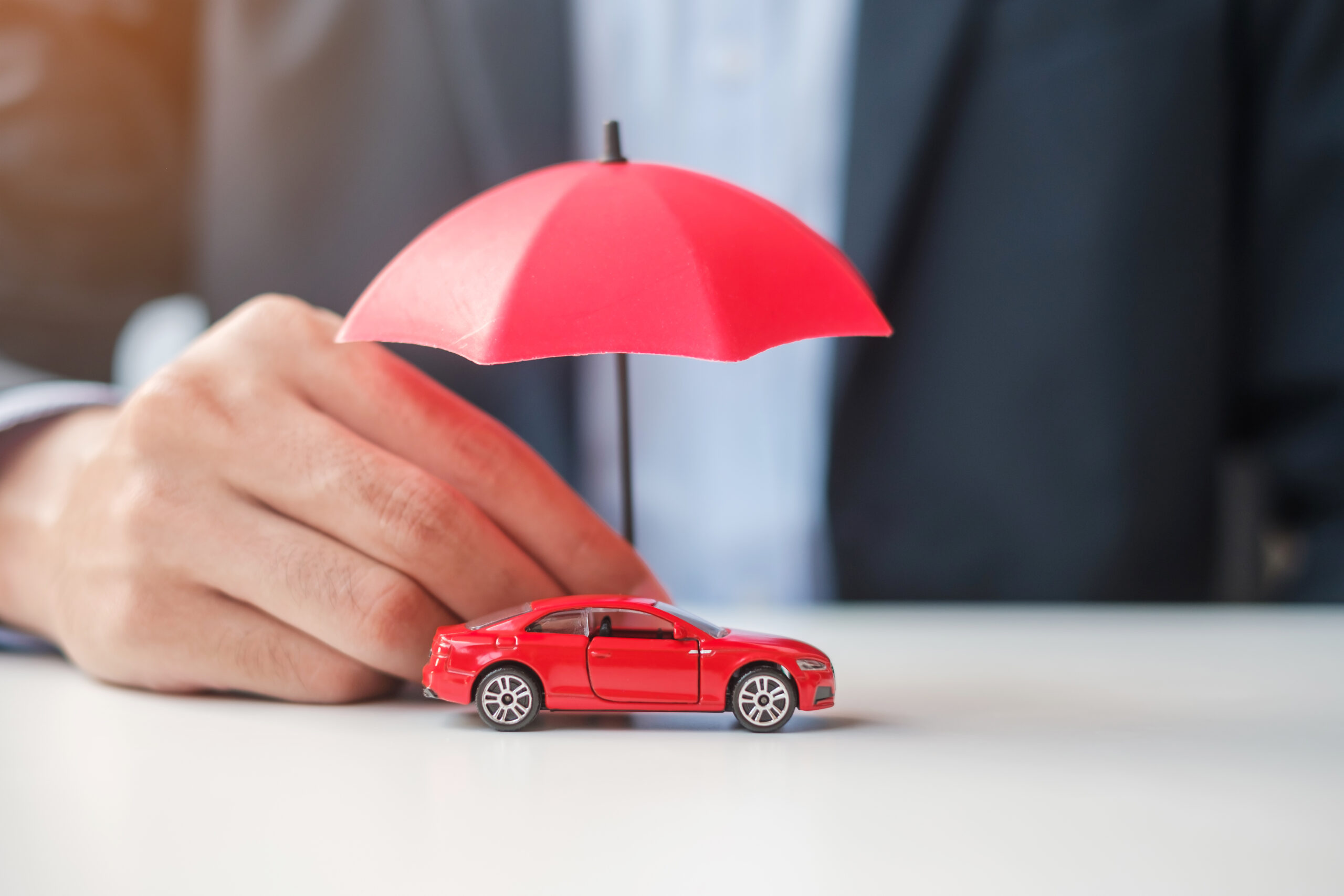 Businessman hand holding umbrella and cover  red car toy on table. Car insurance, warranty, repair, Financial, banking and money concept